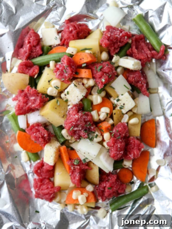 Assembled beef and veggie tin foil dinner packets, tightly sealed and ready for cooking.