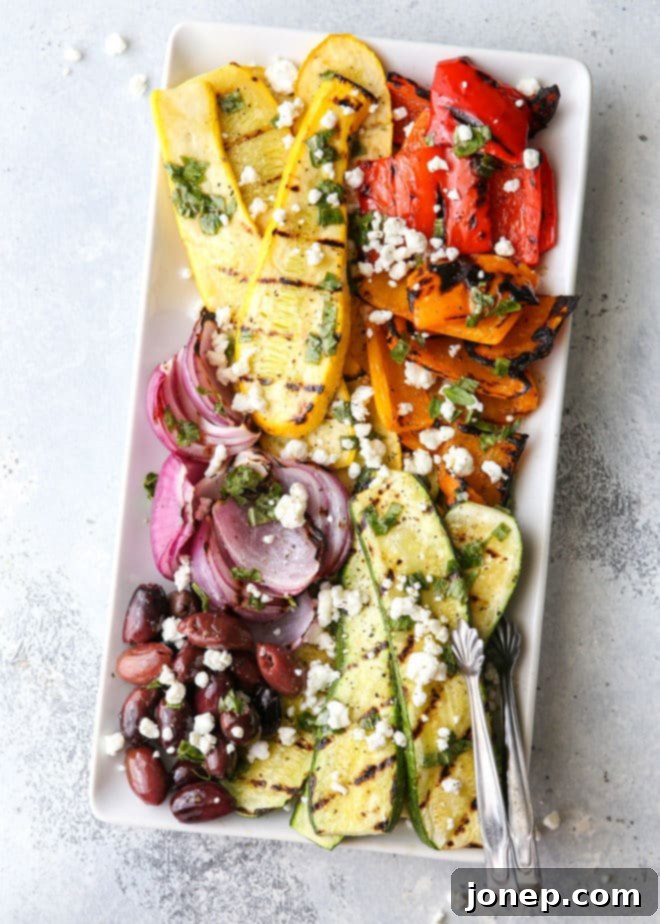 A beautifully arranged grilled vegetable antipasto platter featuring zucchini, summer squash, red onion, and bell peppers, with kalamata olives, goat cheese, and fresh basil dressing, perfect for summer entertaining.