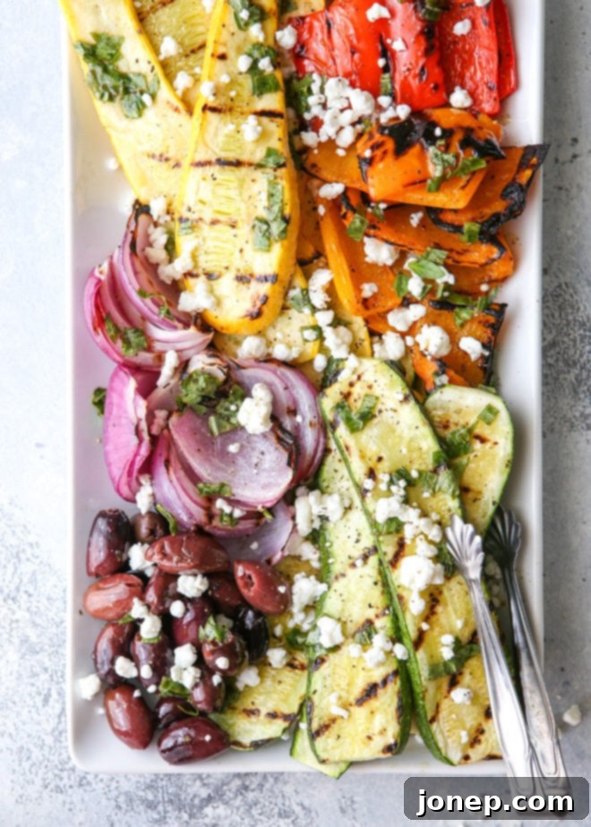Close-up of the fully assembled grilled vegetable antipasto platter, showcasing caramelized vegetables, kalamata olives, crumbled goat cheese, and a fresh basil dressing.