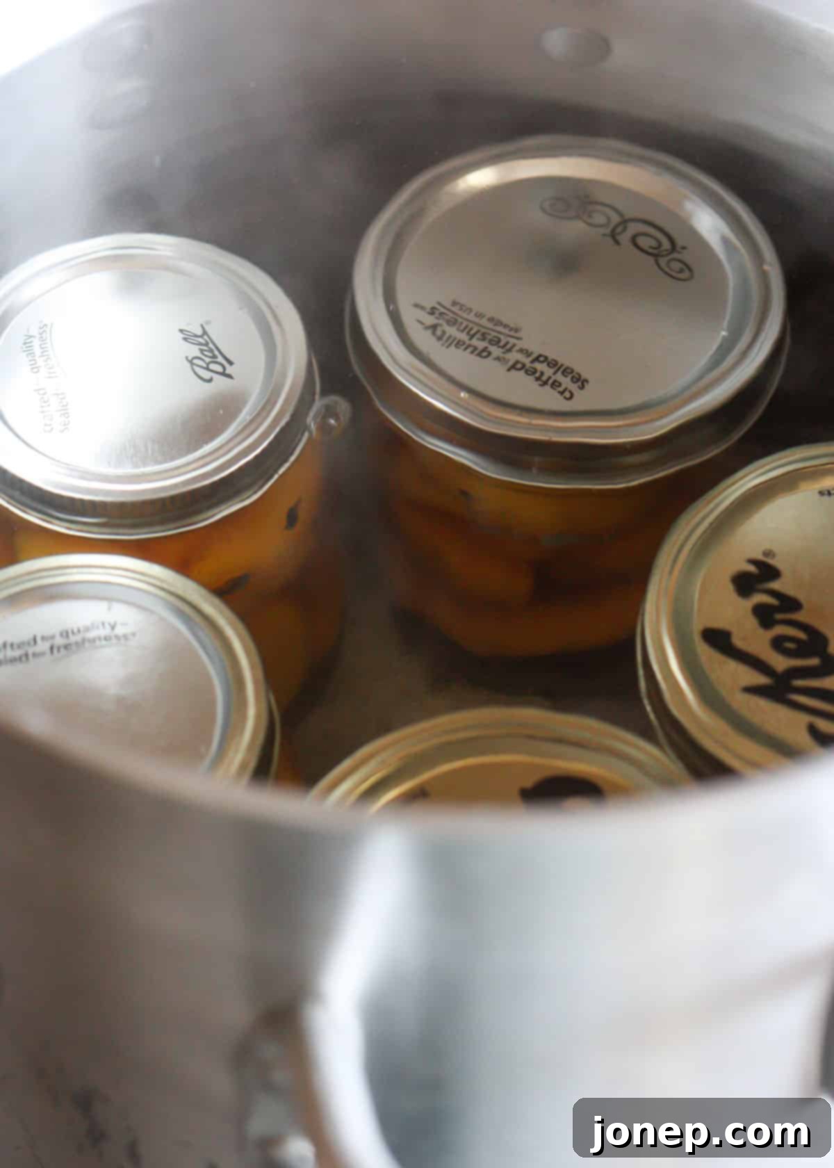 Glass jars of canned peaches submerged in a boiling water bath canner