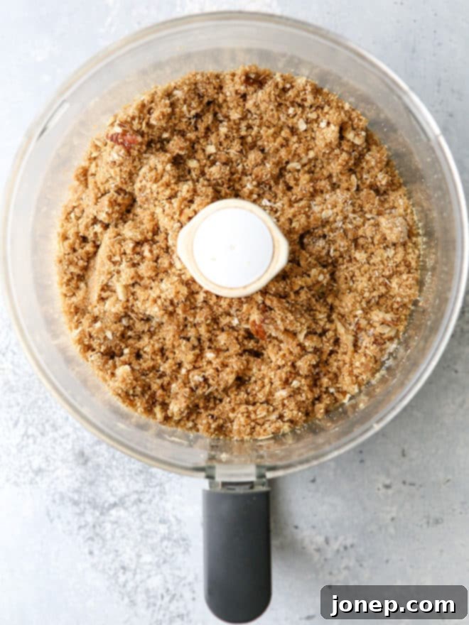 Close-up of graham cracker streusel, showing the rich texture with crushed graham crackers, pecans, and oats, ready to become the crust and topping for cheesecake bars.