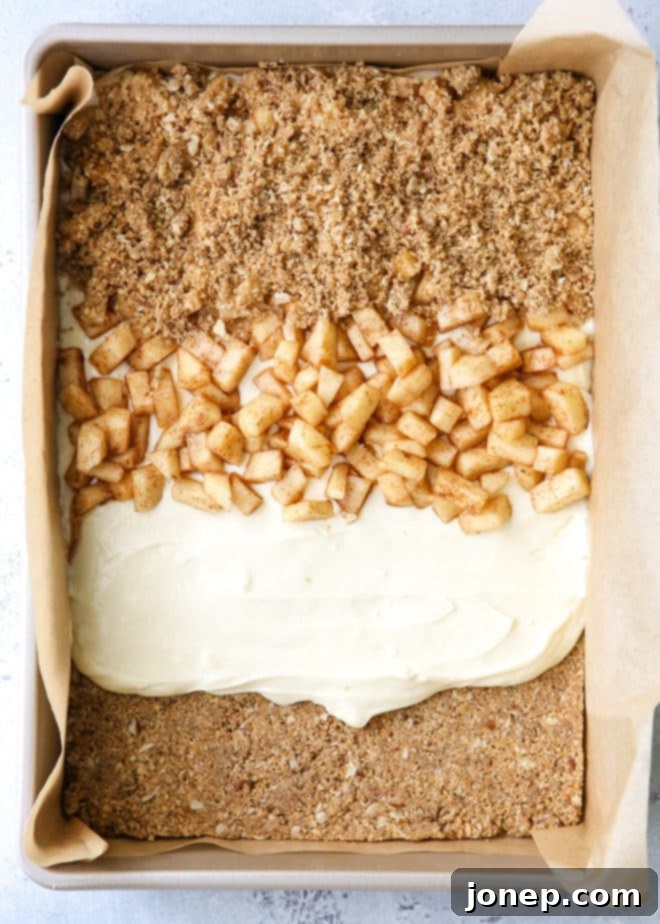 Overhead shot of freshly baked Caramel Apple Cheesecake Bars, showcasing the distinct layers of graham cracker streusel, cream cheese, cinnamon apples, and a generous caramel drizzle, ready to be sliced and served.