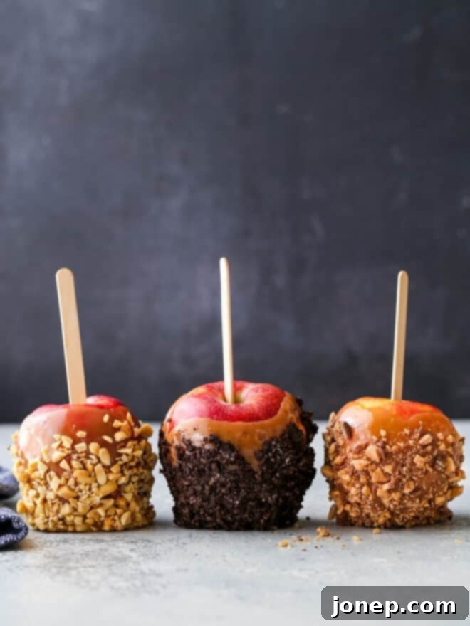 Three homemade caramel apples with various toppings like crushed Oreos, chopped nuts, and sprinkles, displayed on a wooden surface.