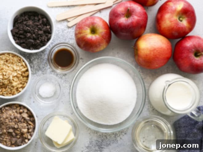 A collection of ingredients for homemade caramel apples laid out on a kitchen counter, including apples, heavy cream, sugar, butter, corn syrup, vanilla, salt, and craft sticks.