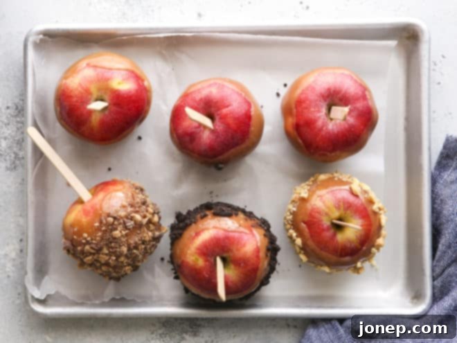Several homemade caramel apples adorned with various toppings including crushed Oreos, chopped nuts, and chocolate drizzle, displayed on wax paper to set.