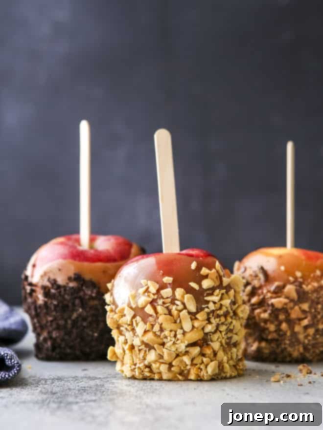 A vibrant close-up of three gourmet caramel apples featuring a variety of toppings: crushed Oreos, chopped nuts, and pieces of candy bar, presented on a rustic wooden board.