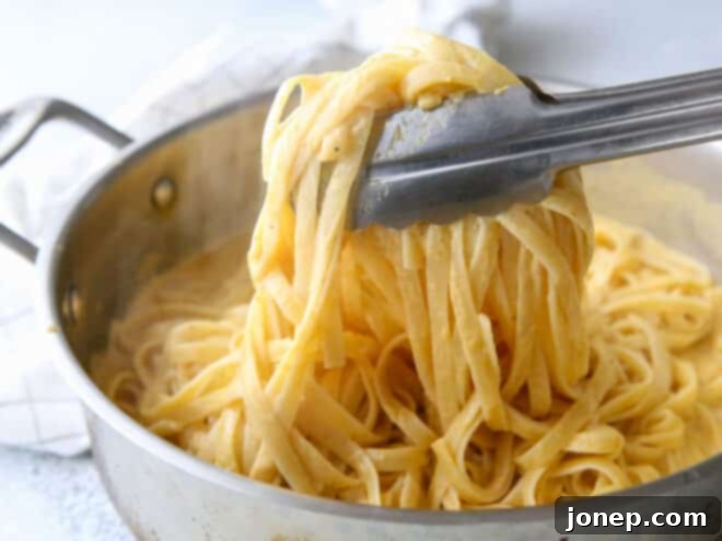 tossing pasta in pumpkin alfredo sauce in pot with tongs