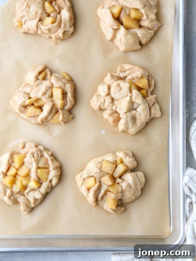 Shaped apple fritters on parchment paper, ready for their second rise and looking puffy