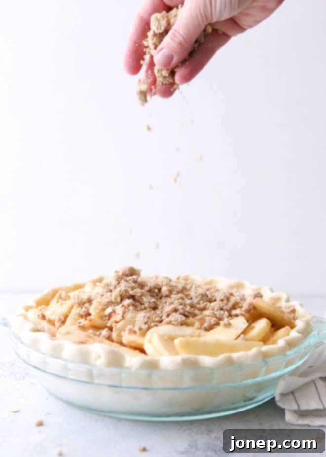Applying the generous pecan and oat crumb topping to the prepared Dutch apple pie filling before baking