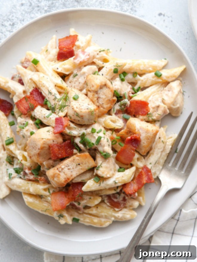 A top-down view of a generous serving of creamy Chicken Bacon Ranch Pasta, garnished with fresh dill and chives, invitingly presented in a rustic bowl.