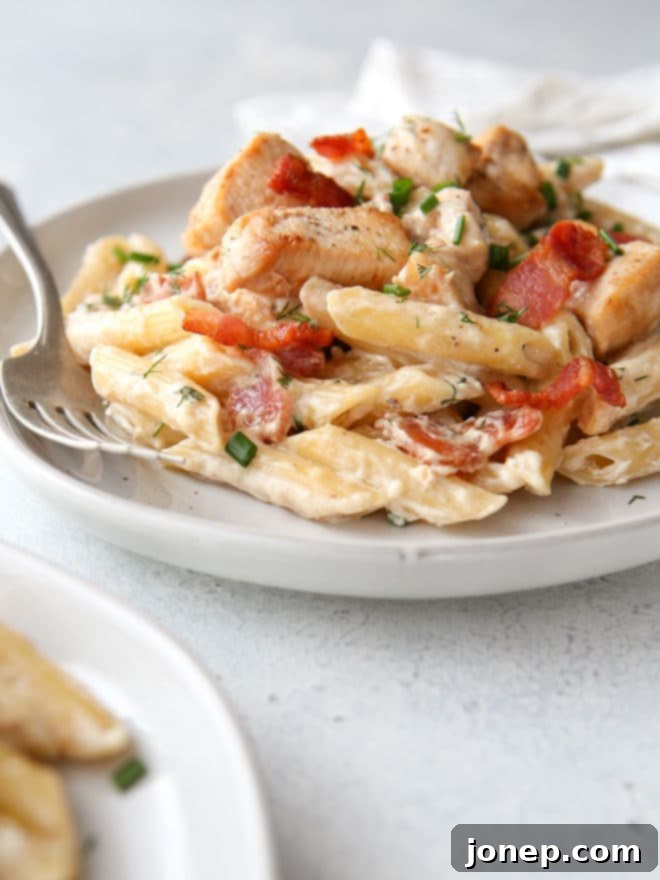 An overhead shot of the delicious Chicken Bacon Ranch Pasta served in a bowl, with a fork ready to enjoy, highlighting the creamy texture and vibrant herbs.
