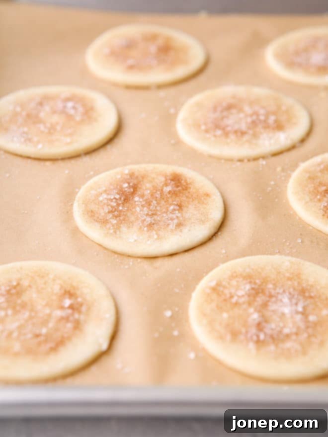 Upcycled Pie Dough Bites 5 Pie crust cutouts with egg wash and cinnamon sugar on a baking sheet, ready for the oven