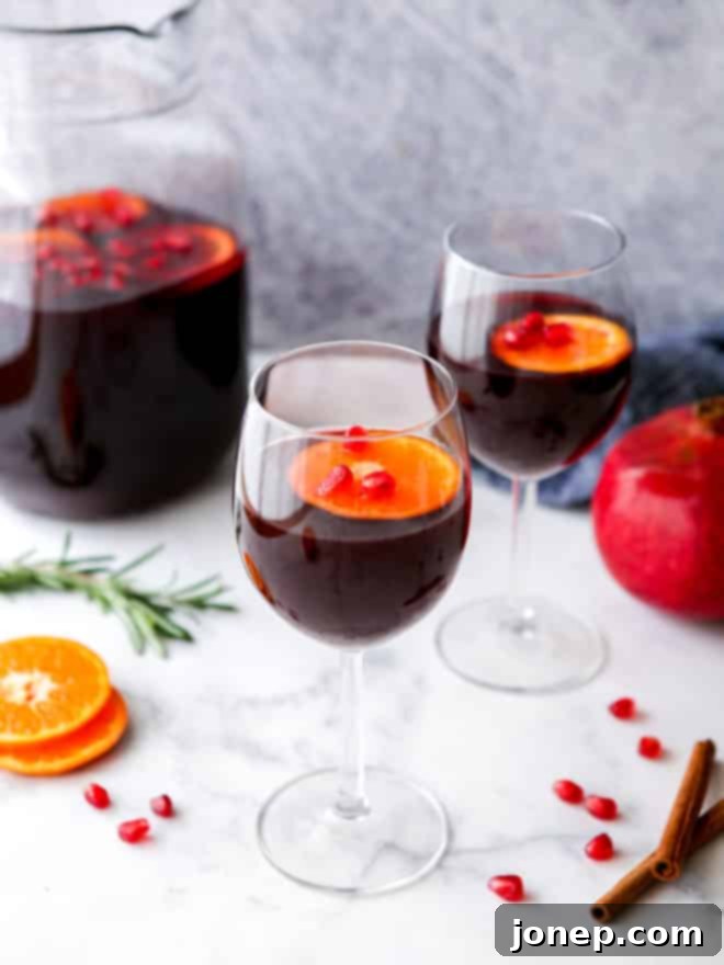 Two glasses filled with vibrant red pomegranate orange winter sangria, garnished with fresh orange slices and pomegranate arils, ready for holiday celebrations