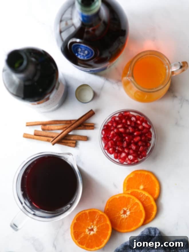 Ingredients laid out for Pomegranate Orange Winter Sangria, including red wine, brandy, juices, fresh pomegranates, and a cinnamon stick