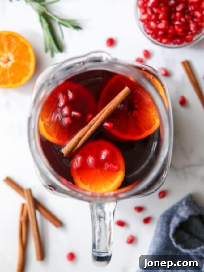 A large pitcher overflowing with freshly mixed pomegranate orange winter sangria, featuring visible fruit slices and cinnamon sticks, chilling for optimal flavor