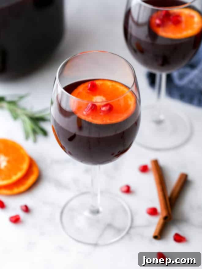 A close-up shot of a single glass of refreshing pomegranate orange winter sangria, showcasing the rich red color, ice, and floating fruit garnishes