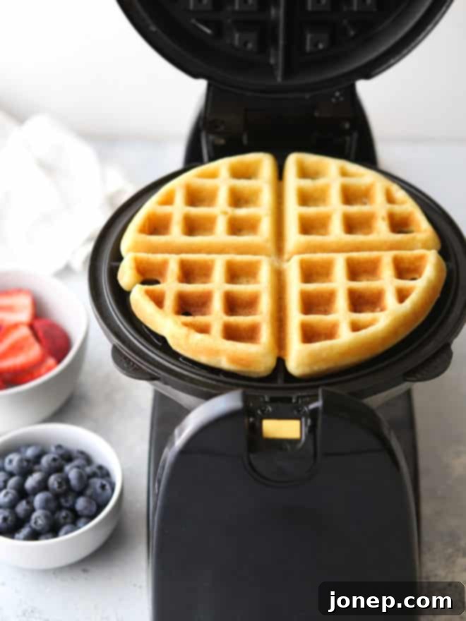Another appealing perspective of a single buttermilk waffle, beautifully golden and richly textured, placed on a pristine white plate, perfectly hinting at its delicious crispness and fluffy interior.