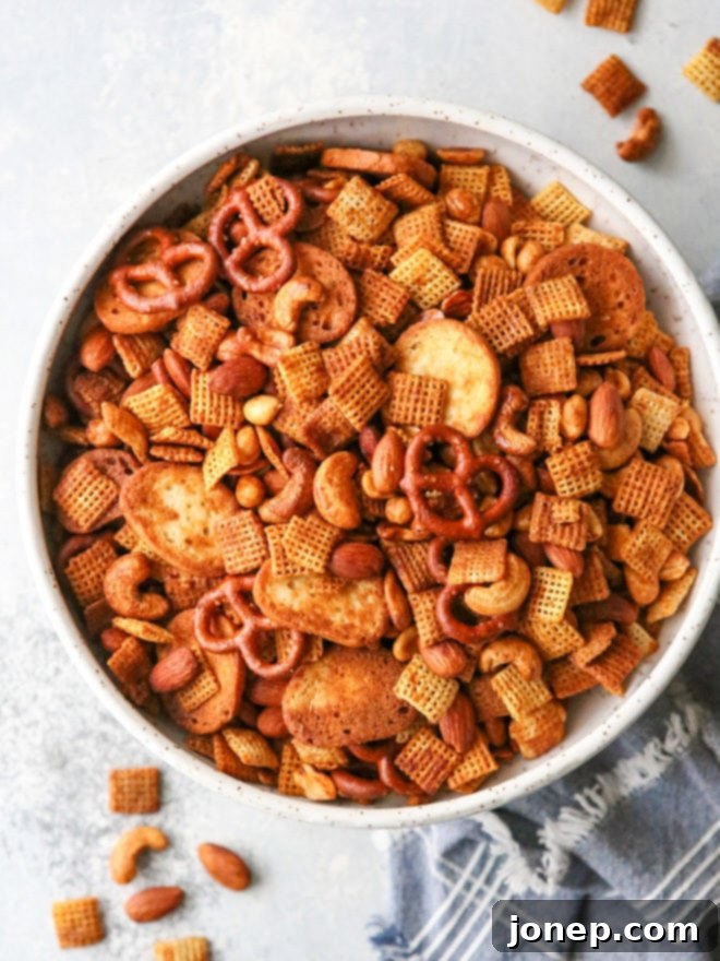 A vibrant bowl of sweet and spicy snack mix featuring Chex cereal, pretzels, bagel chips, and various nuts, glistening with savory glaze.
