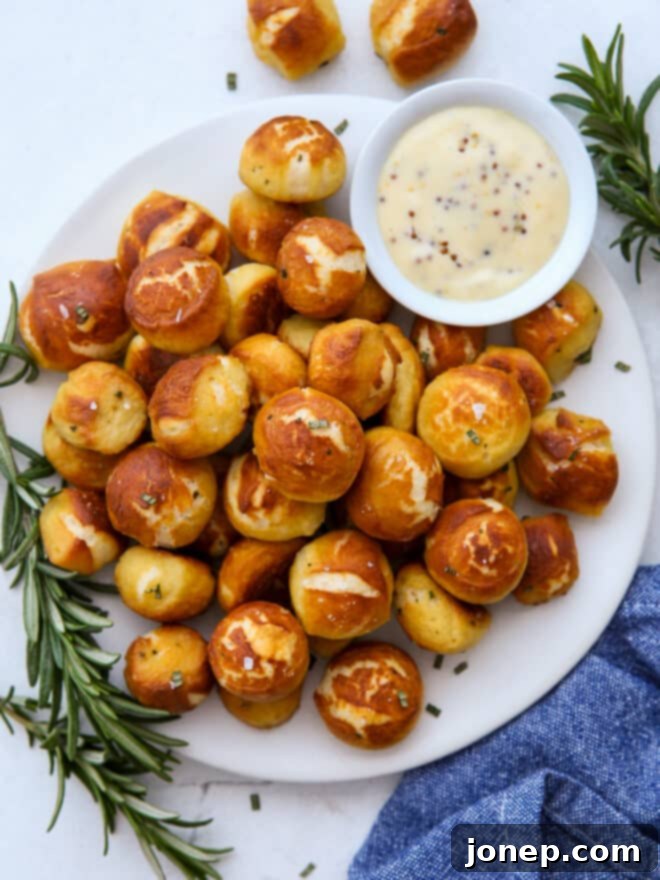 Soft and chewy cheddar and rosemary pretzel bites arranged on a white plate with a small bowl of honey mustard dipping sauce.