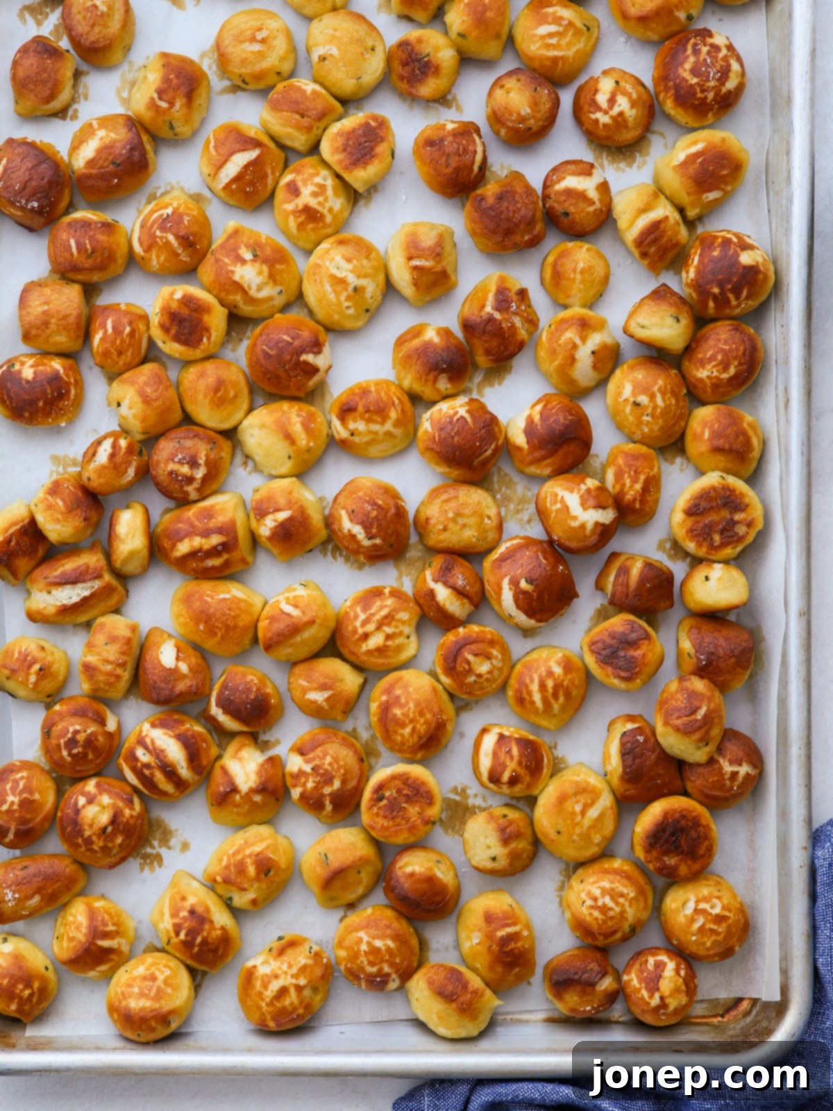 Freshly baked golden brown pretzel bites scattered on a parchment-lined baking sheet.