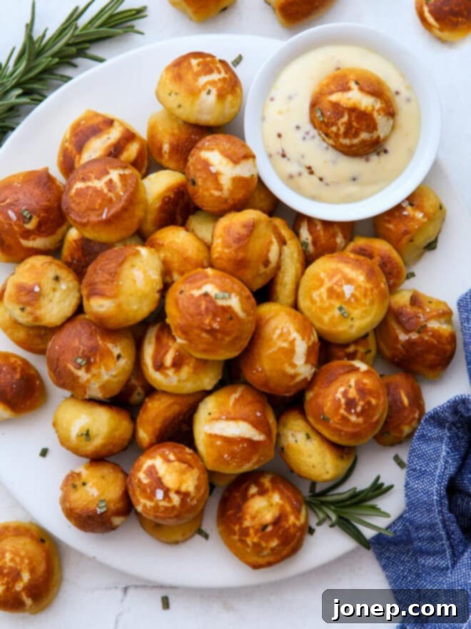 A generous serving of cheddar and rosemary pretzel bites on a plate, with a side of honey mustard sauce, ready for a party.