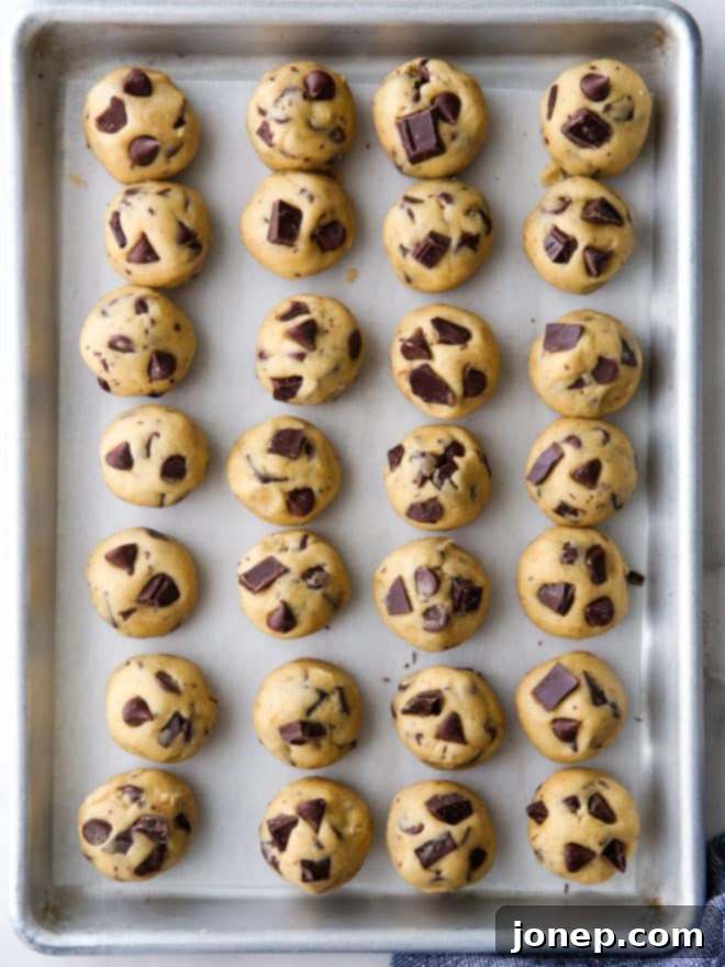 Neatly arranged rounds of chocolate chip cookie dough resting on a sheet pan lined with parchment paper, fresh from being portioned and ready for their essential quick freeze.