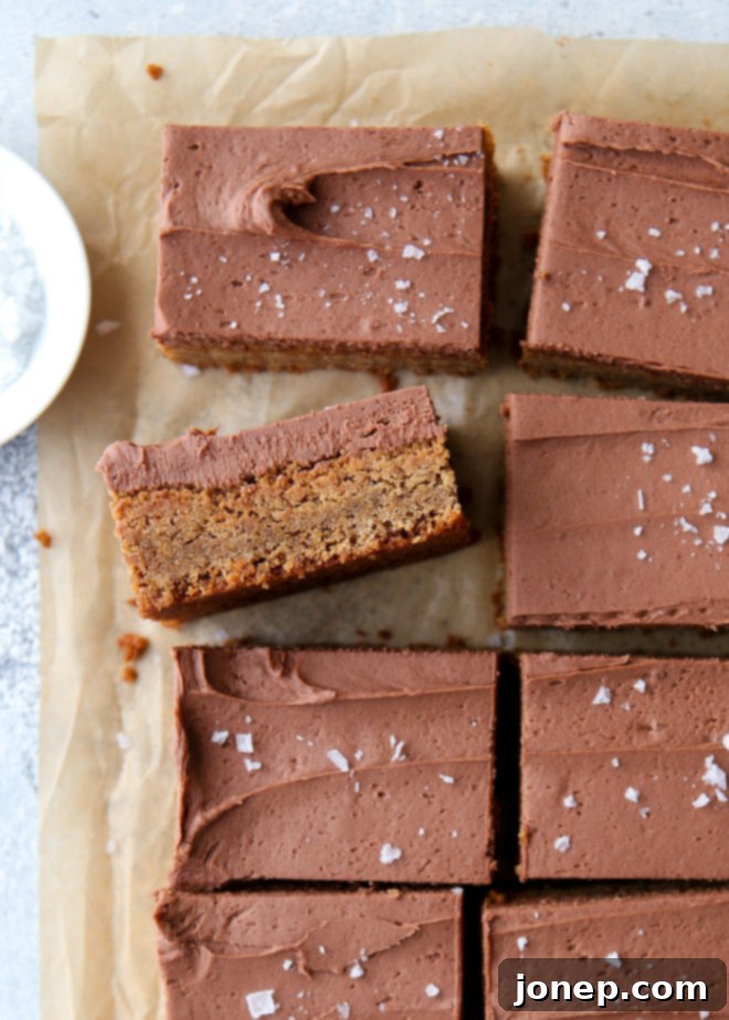 Soft, chewy peanut butter blondies generously topped with thick chocolate buttercream frosting, sliced and ready to serve on a white plate.