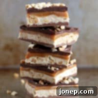 Copycat Snickers Bars 2 A close-up shot of decadent homemade Snickers bars cut into squares, showing off the distinct layers of chocolate, nougat, caramel, and peanuts.