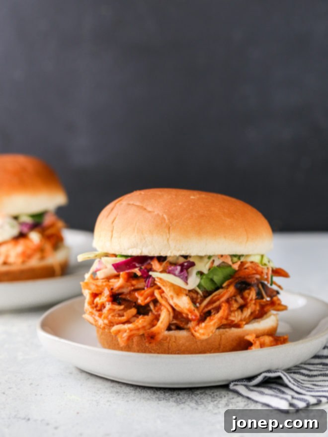Delicious pulled BBQ chicken sandwiches piled high on soft buns with pickles and coleslaw