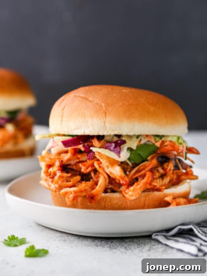 Two freshly made pulled BBQ chicken sandwiches on a platter with sides