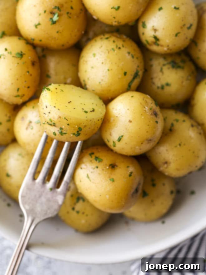 A close-up of a hand holding a fork, taking a perfectly tender, buttery bite of a boiled potato from a serving bowl, highlighting its texture.