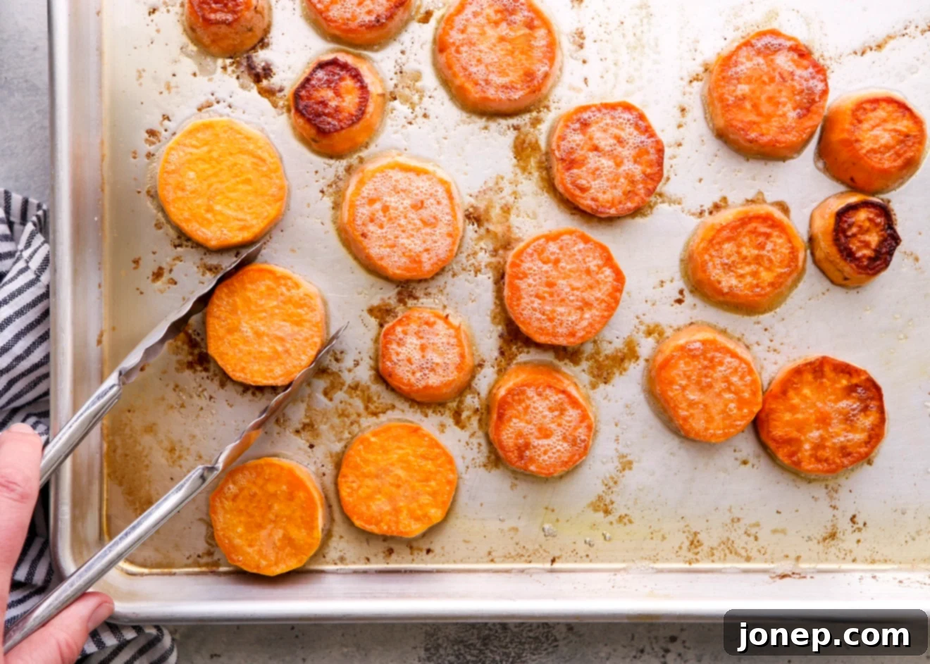 Flipping sweet potatoes on a baking sheet with tongs during roasting