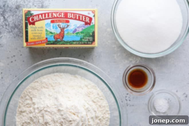 Essential ingredients for shortbread cookies laid out on a wooden surface, including high-quality butter, granulated sugar, vanilla extract, all-purpose flour, and a pinch of salt.