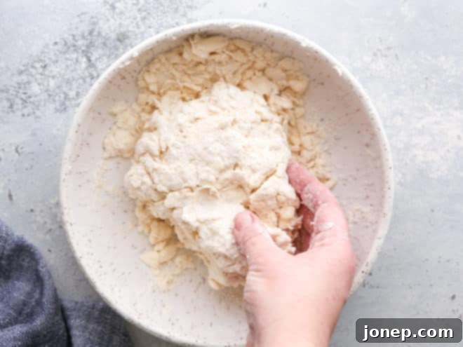 Mixing puff pastry dough by hand to bring it together, showing a shaggy texture.