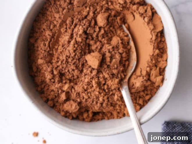 A close-up of natural unsweetened cocoa powder in a ceramic bowl, showing its light reddish-brown hue.