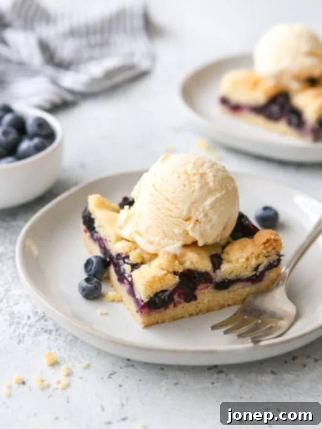 Berry Bliss Bars 2 Delicious blueberry pie bars served with a scoop of vanilla ice cream on a white plate, ready to be enjoyed.