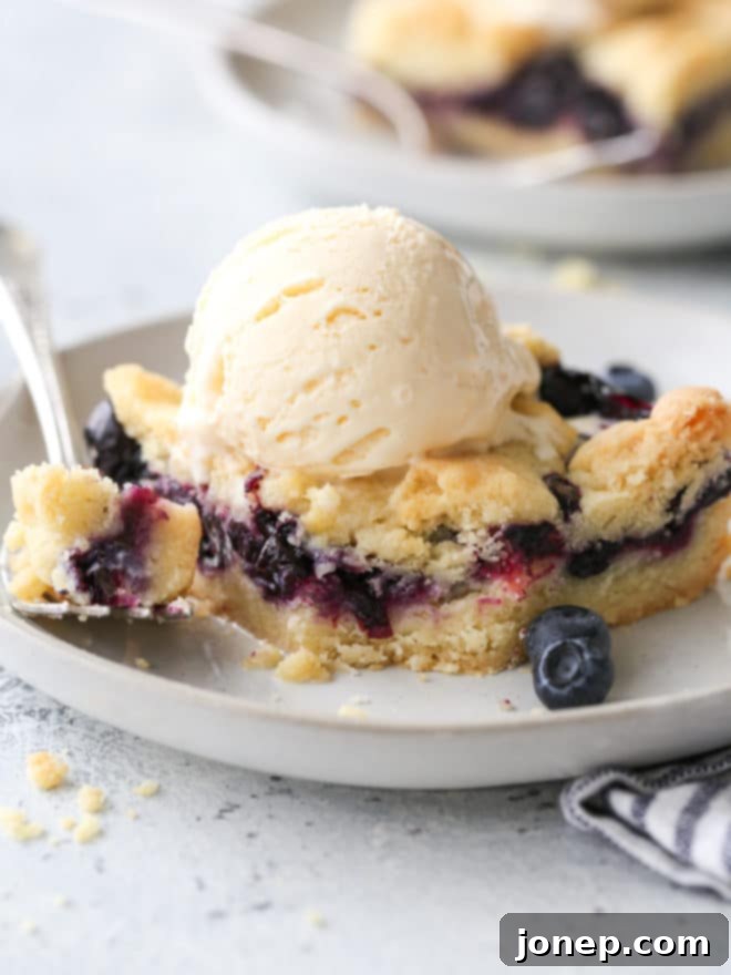 Berry Bliss Bars 7 Close-up of a blueberry pie bar with a bite taken out, showing the juicy blueberry filling and buttery crust, served with ice cream.