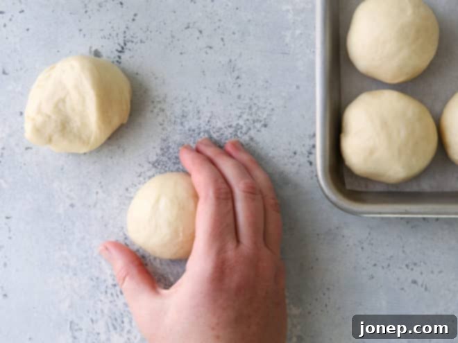 Hands demonstrating the technique of forming traditional round white dinner rolls from dough portions on a lightly floured surface.