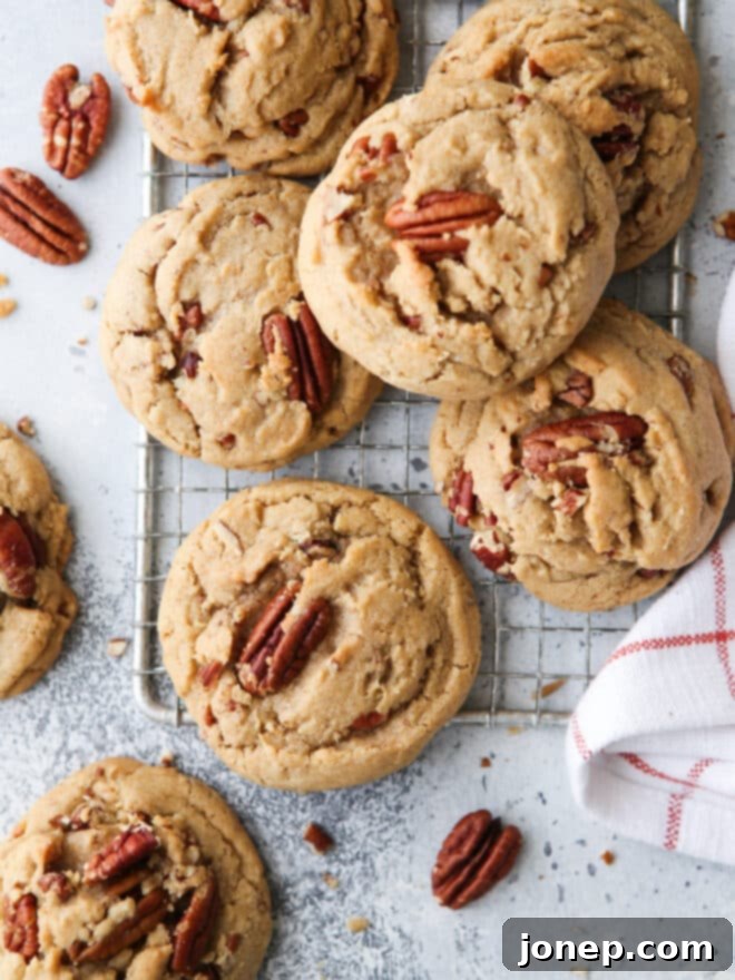 Closeup of golden brown butter pecan cookies on a wire cooling rack, showcasing their chewy texture and prominent pecan pieces.