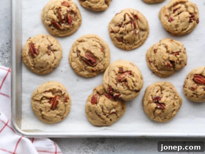 Freshly baked brown butter pecan cookies cooling on a sheet pan lined with parchment paper, showing their golden edges and soft centers.