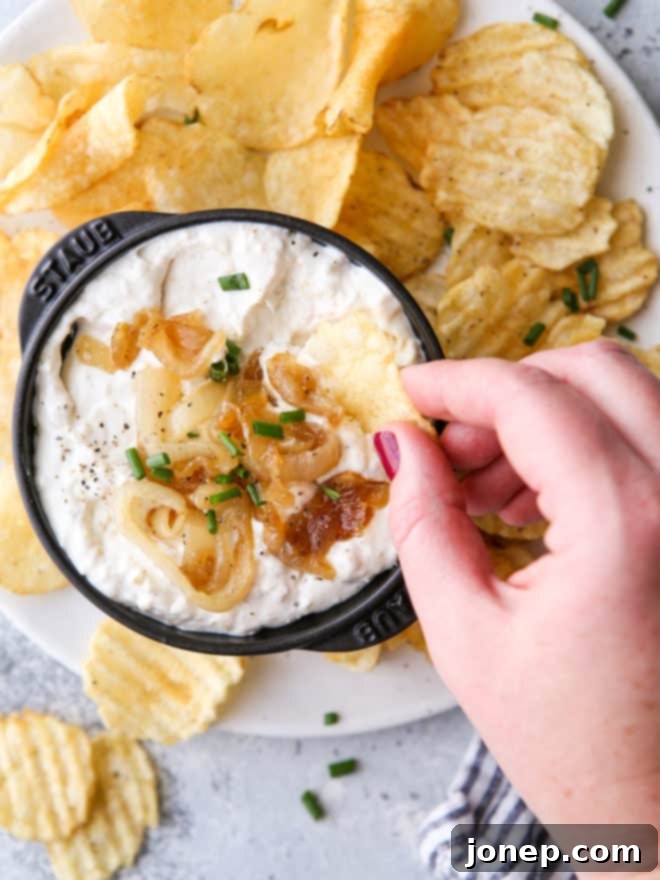 dipping potato chips into a bowl of homemade french onion dip, garnished with chives