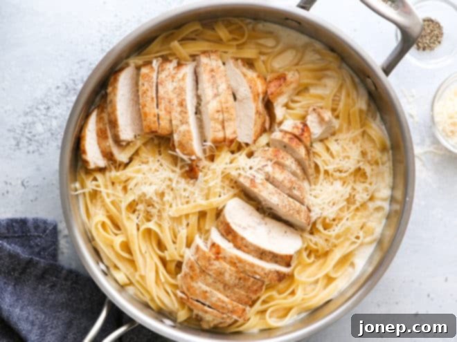 A large skillet filled with creamy chicken fettuccine alfredo being tossed and mixed for even coating.