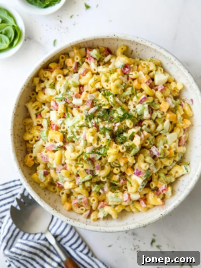 Creamy Classic Macaroni Salad 2 Classic macaroni salad in a serving bowl, garnished with fresh herbs and surrounded by ingredients, perfect for a summer gathering.