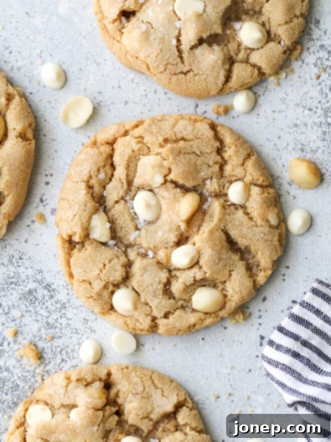 A close-up view of golden-brown white chocolate macadamia nut cookies with visible chunks of chocolate and nuts, stacked on a plate.