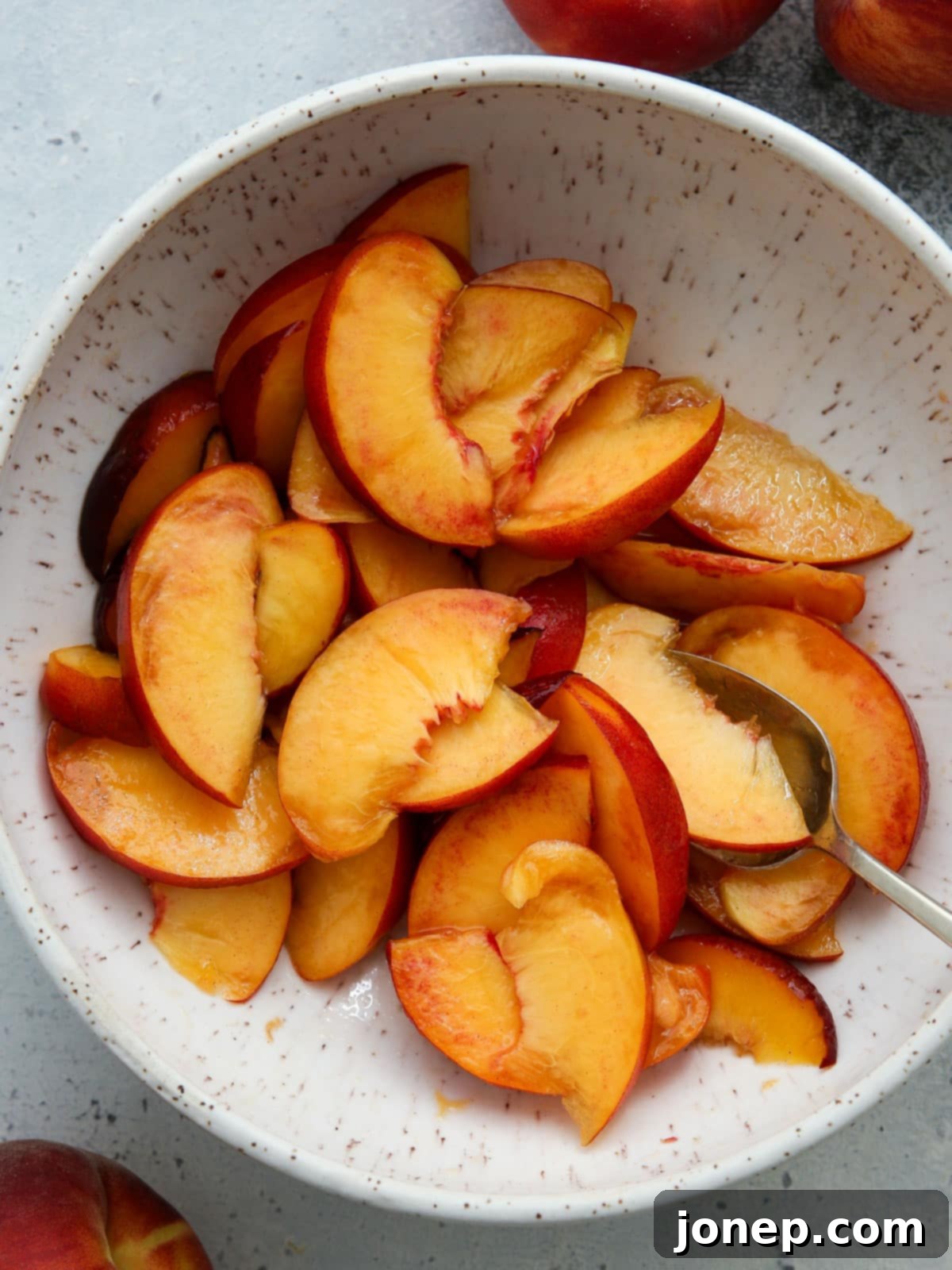 Sliced peaches tossed with sugar and vanilla in a bowl, macerating to become juicy