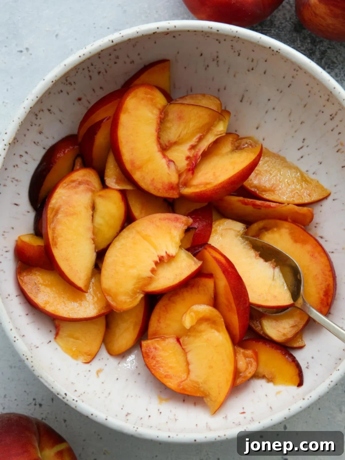 A bowl filled with freshly sliced peaches, glistening with juice after being tossed with sugar and vanilla.