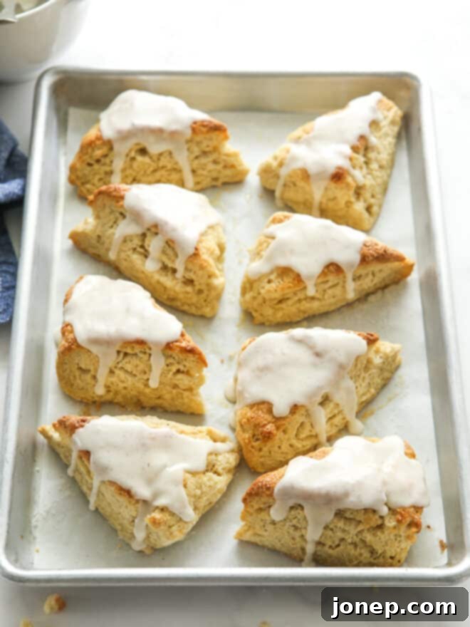 A batch of warm vanilla bean scones, some already glazed, waiting on a baking sheet, ready to be enjoyed.
