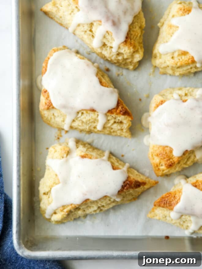 A detailed close-up shot of several vanilla bean scones with frosting, arranged on a baking sheet, highlighting their texture and glaze.
