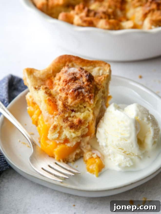 closeup of a slice of peach cobbler pie on a plate, topped with a scoop of vanilla ice cream and a garnish of mint