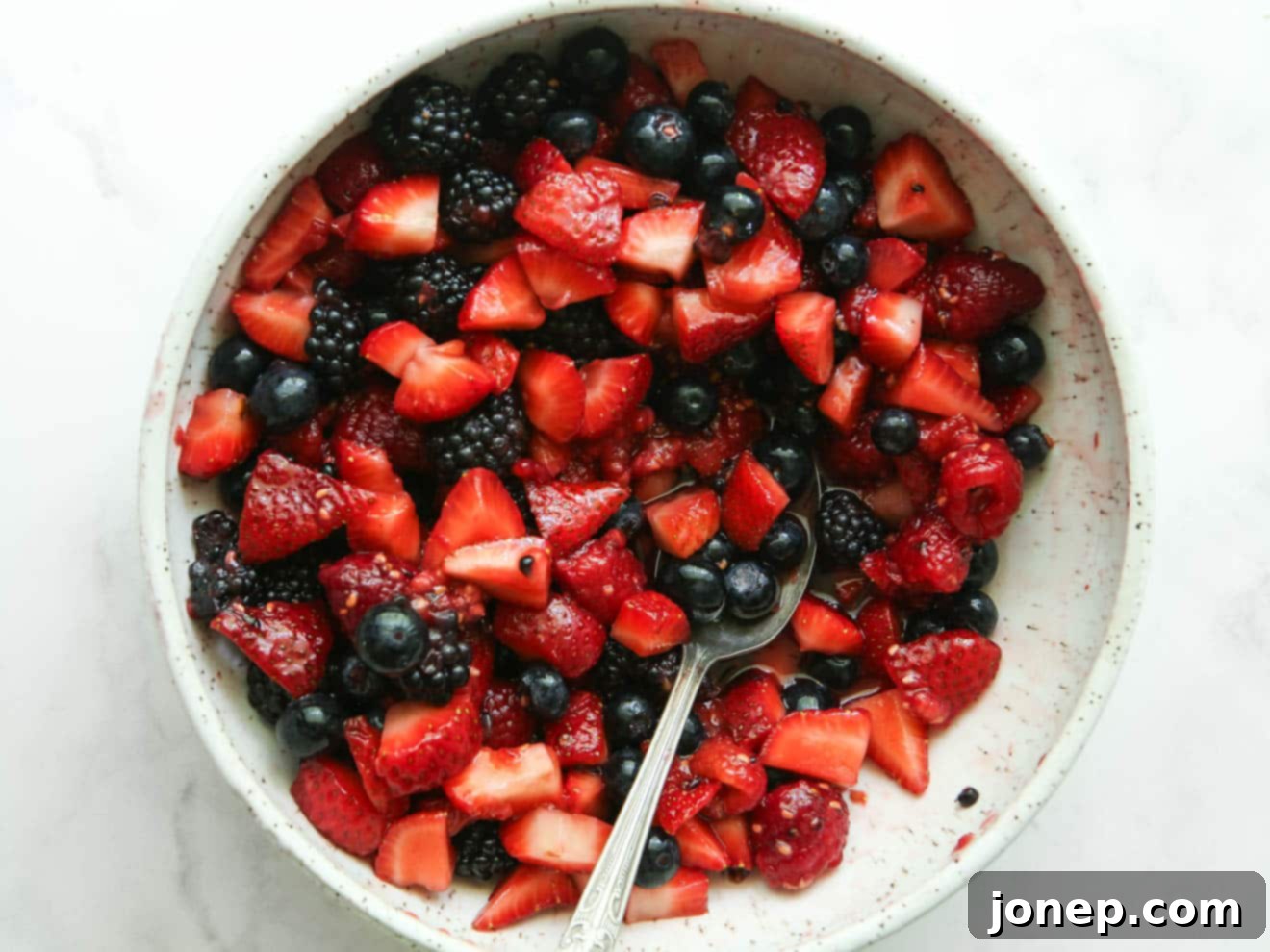 Half of the berries macerated with sugar in a bowl, showing released juices.